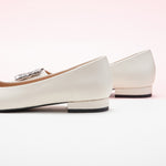 Step into sophistication with these white flats featuring a crystal buckle, perfect for a polished and refined look.